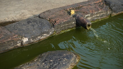 Water flows from a rustic spout into a small pond made of stone blocks
