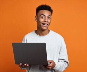 A young person holds a laptop computer, smiling broadly against an orange background, exuding happiness and engagement.