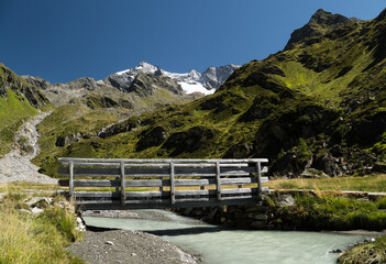 Holzbr&uuml;cke &uuml;ber Gletscherbach im Ahrntal mit Blick auf die Rieserferner-Gruppe