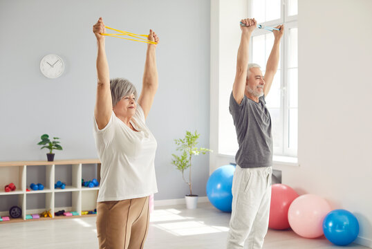Cheerful senior couple doing sport stretching exercises during arm rehabilitation in clinic. Joyful smiling elderly man and woman training together in gym, working on their mobility and wellbeing.