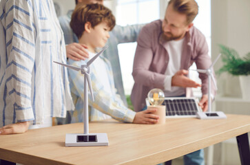 Cropped shot of family learning about renewable energy sources standing near the table. Father is telling to his son about solar panels, wind turbines, photovoltaic energy and environmental protection