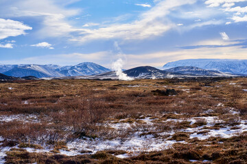 Landscape view of Icelands geothermal area showcasing colorful minerals, steaming vents, and barren landscapes under bright blue skies at Hverir.