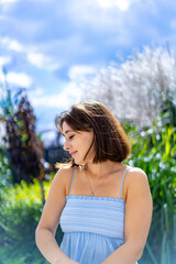 Naklejka premium Young woman enjoying a sunny day in the garden. A woman in a blue dress stands in a vibrant garden, basking in the warmth of the sun and feeling serene.