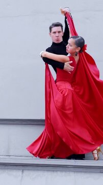 Dancers showcase an intense tango performance, wearing flowing red costumes that accentuate their movements, set against a neutral backdrop, capturing the energy and elegance of dance