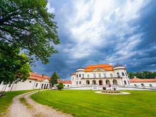 Historic mansion under dramatic cloudy sky. A grand mansion stands amidst lush greenery under a swirling sky, showcasing elegant architecture and a scenic pathway.