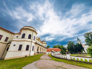 Obraz premium Beautiful architecture under dramatic sky in town. A stunning building with unique design stands by a pathway, surrounded by greenery and an overcast sky, in a quiet town.