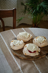 Pavlova cake with strawberry cream and mascarpone. Side view, wooden board, tablecloth, potted flowers in the background. Dessert, aesthetics