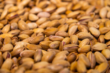 A large pile of unpeeled pistachios, hundreds of them. Close-up
