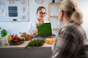 Nutritionist doctor and overweight patient discussing something with green screen on laptop in diet food clinic.