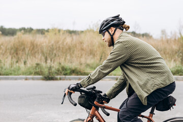Young bearded man in helmet and casual clothes riding bicycle to work.