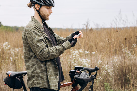 Man cyclist standing in a field using smartphone. Concept of outdoor technology.