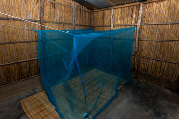Reed-Walled African House with Blue Mosquito Net over Traditional Reed Mat