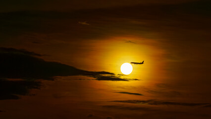 Tokyo, Japan - Oct 2 2024, Panoramic view of the bright orange sunset sun among dark clouds, silhouette of an airplane flies past the sun, Tokyo, Japan