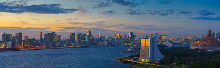 Tokyo, Japan - Oct 2 2024, panoramic aerial view of Tokyo Bay cityscape in background and the Rainbow Bridge, in the foreground is a part of Odaiba Island with a triangular building, Tokyo, Japan