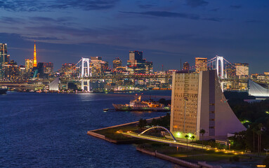 Tokyo, Japan - Oct 2 2024, panoramic aerial view of Tokyo Bay cityscape in background and the Rainbow Bridge, in the foreground is a part of Odaiba Island with a triangular building, Tokyo, Japan