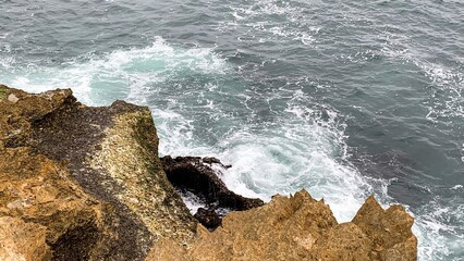 Rocky cliffs embrace roaring waves, evoking adventure and tranquility for World Oceans Day and maritime folklore celebrations