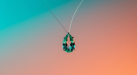 Obraz premium A teardropshaped green gem pendant suspended by thin strings against a gradient of teal and orange