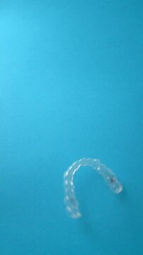 Clear dental aligner falling on blue background. Orthodontic slow motion vertical video.