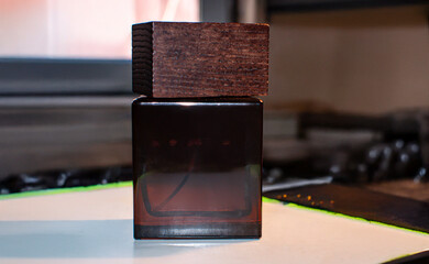 Perfume bottle. The bottle is a dark, amber-colored glass cube with a prominent, textured wooden cap