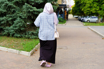 Woman walking on a city sidewalk wearing a headscarf and casual outfit during midday