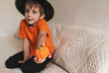 Boy 6 years old in wizard hat, magician playing with pumpkin on halloween at home on white background. Minimalism, flags orange color