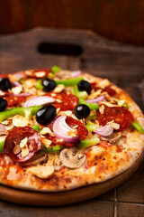 Pizza with chorizo ​​sausage, mozzarella cheese, green pepper and black olives. Rustic wooden background. Soft focus.	