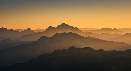 Obraz premium Majestic mountain range during golden hour sunrise, layered peaks with atmospheric haze, warm golden lighting, dramatic landscape photography, nature adventure concept, commercial travel imagery