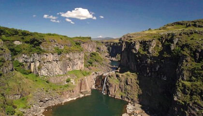 High-angle view of a waterfall cascading into a pool, surrounded by dramatic cliffs and lush greenery