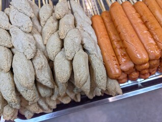 High-angle view of a food stall or buffet tray with light-colored fish balls and bright red sausages on skewers side by side.