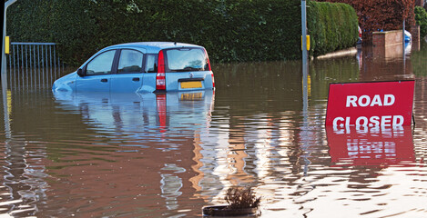 A Road Closed sign nearly underwater with a flooded car nearby. 