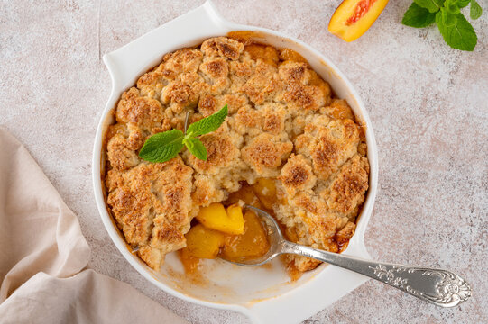 Homemade summer peach cobbler. Pie with juicy peaches, a scoop of vanilla ice cream and fresh mint on a white plate. Comfort food.