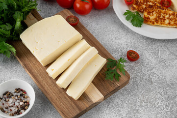 White cheese halloumi on a wooden board with herbs and tomatoes on a concrete background. Top view.