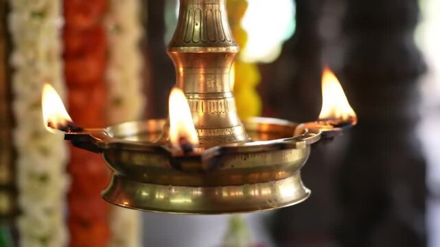 A traditional brass oil lamp with three lit wicks burning brightly during a religious ceremony or festival.