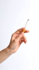 Hand holding a small, metallic key with an orange handle against a plain background