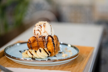 Honey Toast, a square toast baking with butter and topped with vanilla ice cream and chocolate sauce served with banana on blue plate.