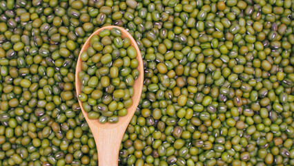 Raw green mung beans on wooden spoon over heap of mung beans background. Perfect for illustrating legumes, natural food ingredients