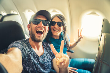 Smiling couple taking selfie inside airplane during flight, showing joy, freedom and travel lifestyle concept