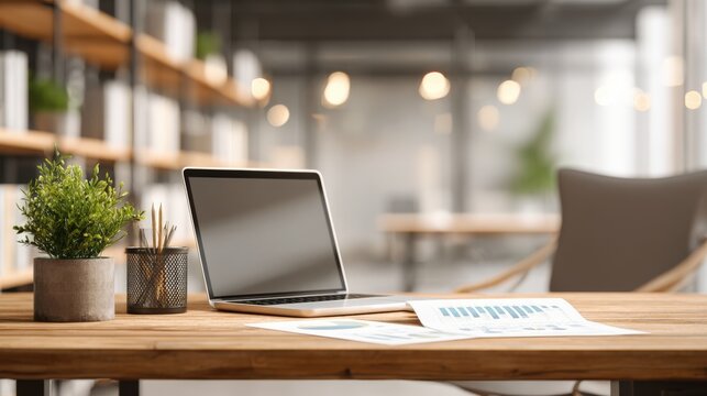 Modern Office Workspace with Laptop, Potted Plant, and Financial Documents on a Wooden Desk