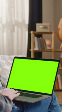 Man sitting with laptop on knees, green screen display for replacement, working or browsing at home on bed. Male person using computer indoors, mockup screen for app or website design.