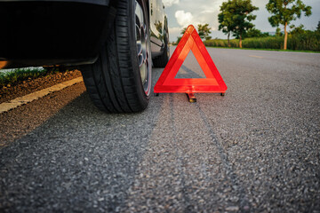 Red triangle emergency stop sign on the road with a broken down vehicle on the side of the road