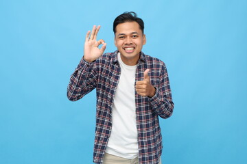 Handsome young Asian man wearing casual clothes, showing ok sign hand gesture and thumbs up,...