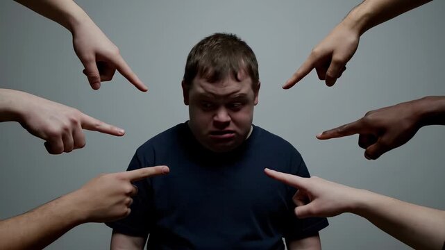 A man with Down syndrome is being pointed at by multiple hands. It is a sad and emotional portrait. Social exclusion, discrimination, bullying.