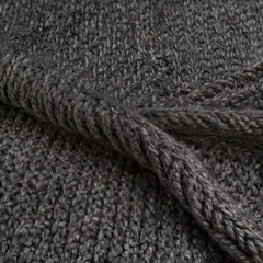 Close-up shot of soft grey knitted fabric, showcasing the intricate textures and detailed patterns. The folds in the fabric create dynamic shadows and depth.