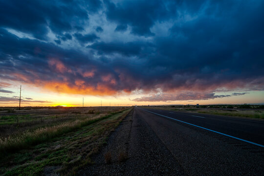 Vibrant sunset over an open highway in a rural Texas with dramatic clouds on a warm evening - Powered by Adobe