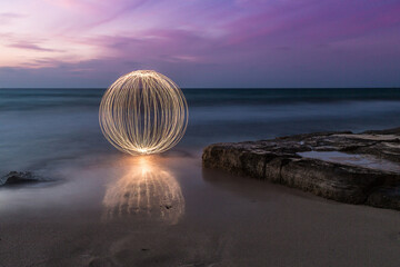 Light painting orb on a tranquil beach at twilight, long exposure photography.
