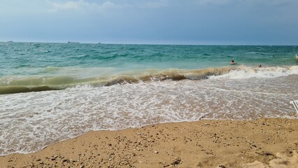 A serene beach scene with gentle waves lapping at the sandy shore. Clear blue water meets the golden sand under a cloudy sky. Ideal for relaxation and vacation concepts.