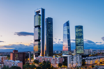 Cityscape of Madrid’s financial district at dusk, featuring modern skyscrapers illuminated...