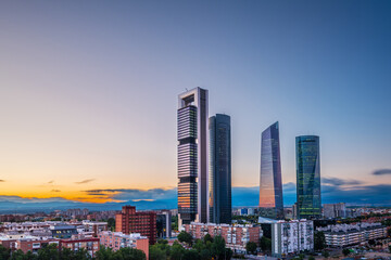 Cityscape of Madrid&rsquo;s financial district at dusk, featuring modern skyscrapers illuminated against the fading evening sky.