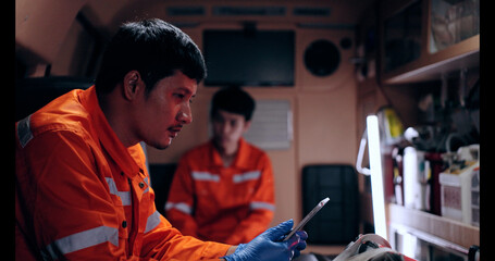 Asian man emergency medical technician (EMT) or paramedic nurse using tablet in ambulance car
