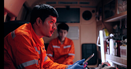 Asian man emergency medical technician (EMT) or paramedic nurse using tablet in ambulance car